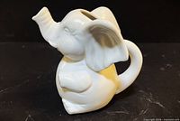 Front left view of white porcelain elephant creamer showing trunk spout, handle tail