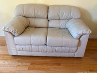 Front view of beige leather loveseat showing seats, back cushions and armrests