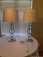 Pair of chrome ring-column table lamps on table with shades visible