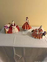 Group shot of all three Royal Doulton Victorian lady figurines on table