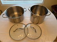 Both stainless stock pots and both lids displayed on table