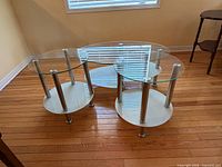 Front view of oval coffee table and two matching round end tables showing glass tops, chrome legs, white shelves