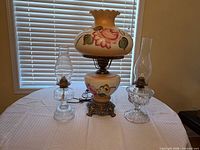 All three lamps on table: large hand-painted electric hurricane lamp centered between two clear glass oil lamps