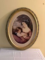 Full view of framed print on wall showing oval gilt frame and mat