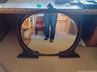 Full view of mirror showing oval shape, carved wood frame and bracket feet