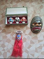 Group shot showing boxed miniature masks, wood wall mask, and tassel ornament
