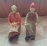 Front view of both carved wooden elder figurines seated in rocking chairs