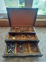 Open jewellery box showing interior compartments filled with assorted costume jewellery
