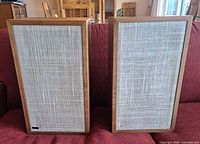 Front view of both speakers showing walnut veneer frames and beige cloth grilles