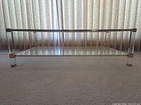 full side view showing glass top, lower shelf, acrylic legs, gold-tone trim