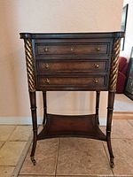 Front view showing drawers, gilt spiral columns, lower shelf and casters