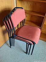 Four stacked chairs showing black frames and burnt orange upholstery