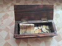 Wooden box open showing folded banknote and coins