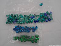 Three clear bags containing assorted green and blue beads displayed on white background