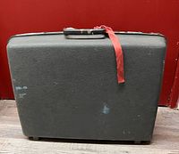 Front view of suitcase showing exterior texture, feet, ribbon on handle