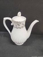 Full side view showing swirl body, floral band, lid with loop finial