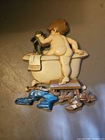 Front view of painted cast metal wall plaque showing child, frog, bathtub, boots and stool