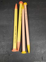 Four straight plastic knitting needles two yellow two peach-pink with capped ends