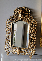 Front view of ornate tabletop mirror showing gilt openwork frame and figural crest