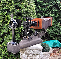Full side view showing wooden bellows camera, lens housing, and cast iron base
