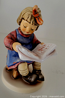 Front view of girl reading figurine showing face, book, attire