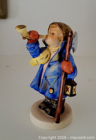 Front view of figurine showing boy blowing horn, staff with lantern and axe head