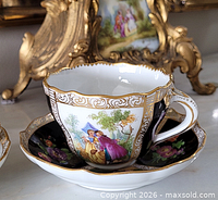 Front view of teacup on saucer showing painted scene, black panels and gold trim