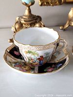 Teacup resting in saucer showing courting scene and gilt detail