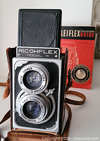 Front view of Ricohflex Model VI camera in leather case with both lenses visible and Rolleiflex Guide in background