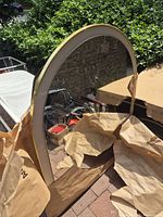 Full view of arched gold-tone mirror leaning outdoors