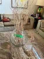 Full view of clear round glass vase with beige decorative branches on table