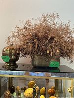 Dried arrangement in metal planter beside brass urn on shelf
