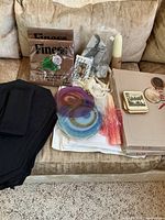 All items grouped on sofa showing placemats box, coasters, candles, napkins, rope tassel, black linens
