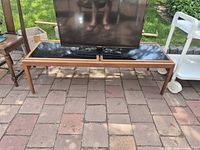 Front view of teak TV stand with black inlay top and television for scale