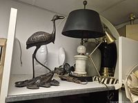 Shelf view showing crane statue, marble lamp with shade, black ceramic lamp body behind, ceramic fish vases and loose wiring