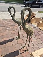 Front view of both metal crane statues standing on brick patio