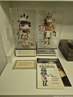 Both Kachina dolls in cases with certificate and book visible
