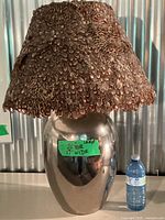 Full view of lamp with metal base and feather shade beside water bottle for scale