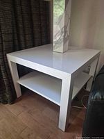 Overall view of white square end table positioned beside curtain and sofa
