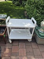 Front angled view of two-tier white plastic serving cart showing handles, shelves and casters