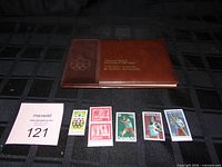 Closed brown Olympic Stamp Souvenir Collection album with five loose stamps displayed