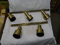 Two brass track light bars with four cylindrical heads displayed on cloth backdrop