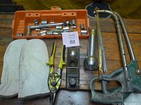 All items laid out on table: socket set, gloves, snips, plane, flashlight, hacksaws