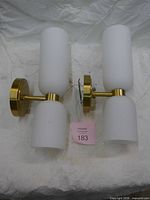 Pair of brass wall sconces showing front view with white cylindrical glass shades and round wall plates