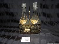 Front view of two diamond-pattern glass decanters with stoppers inside gold-tone lattice carrier; labels visible