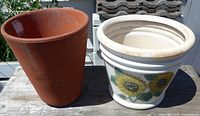 Terracotta pot and white sunflower ceramic pot side by side on wooden surface
