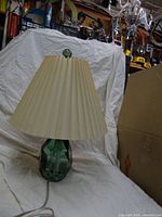 Full view of lamp showing green glass base, beige pleated shade, power cord