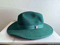Front view of green wool felt fedora showing crown, brim, band and logo pin