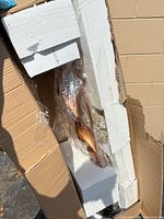 Sculpture partially visible inside shipping box with foam and plastic wrap