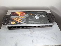 Outset cast iron shrimp pan with packaging sleeve visible on marble surface